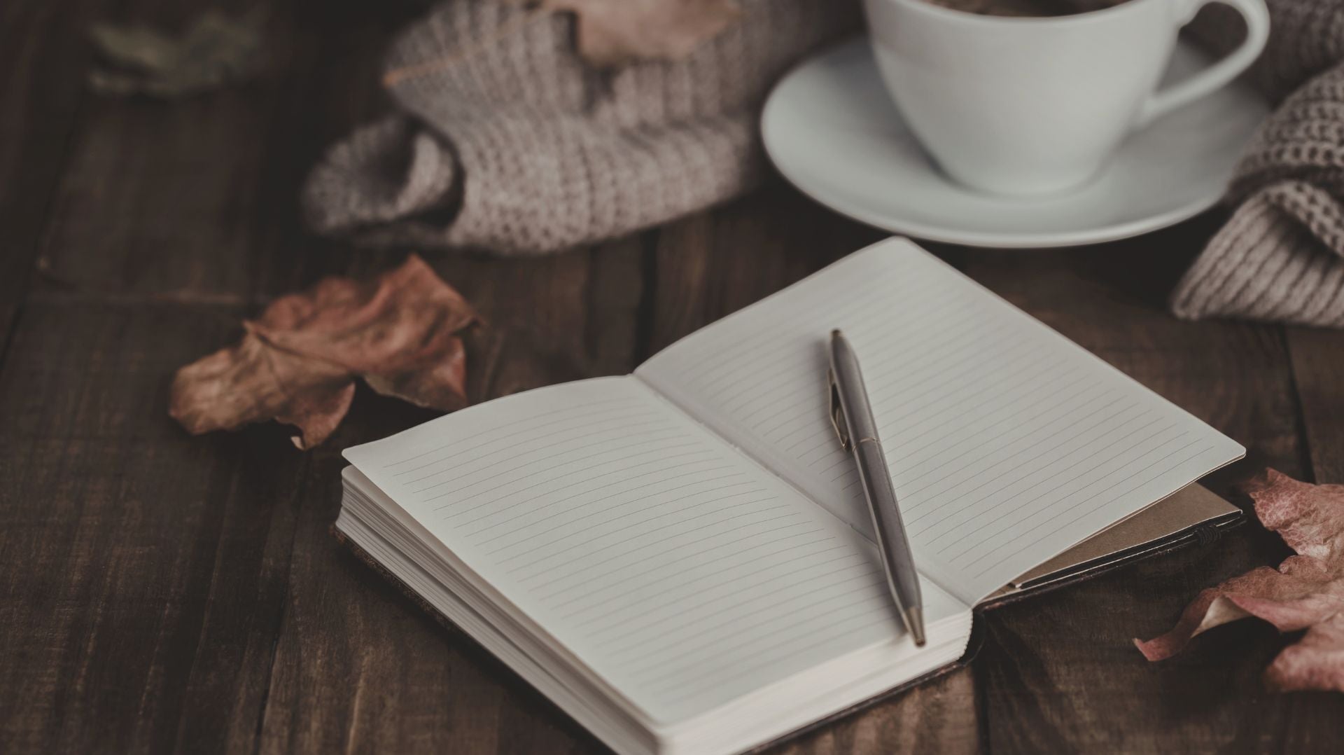 Open lined journal with pen beside a warm drink on a wooden table