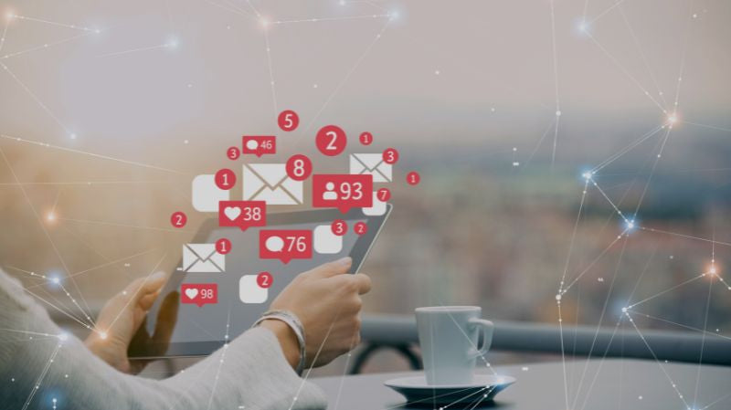 Person holding a smartphone with social media notification icons beside a cup of coffee