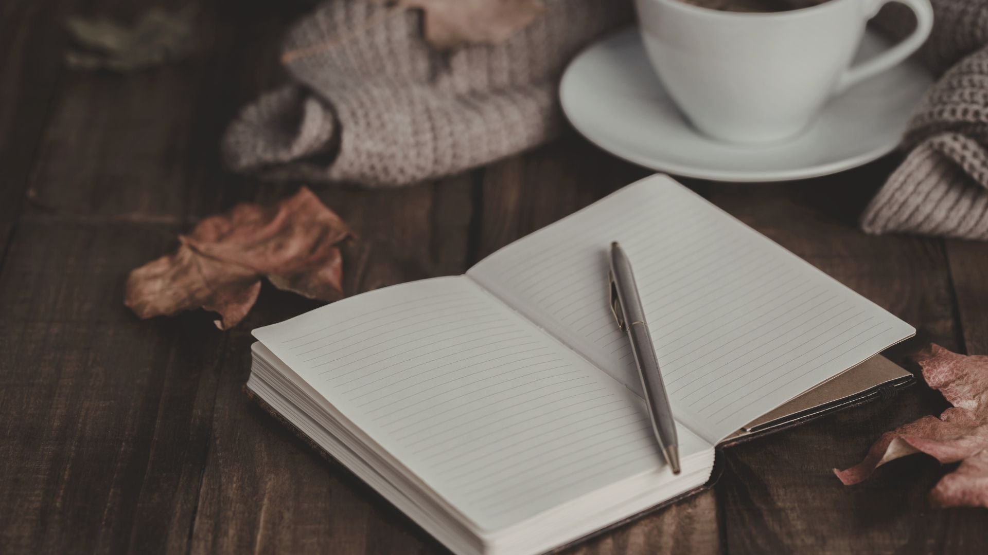Open lined journal with pen beside a warm drink on a wooden table