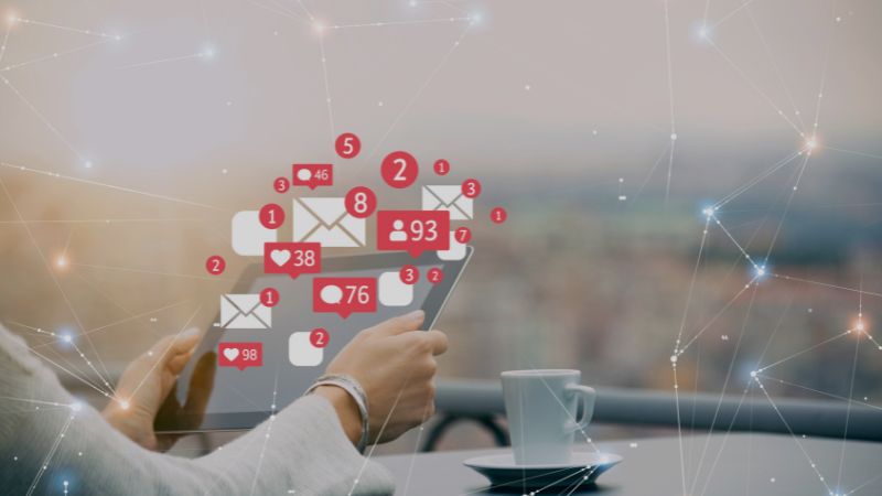 Person holding a smartphone with social media notification icons beside a cup of coffee